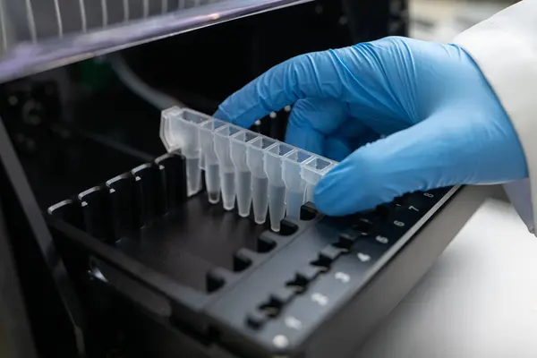 Laboratuvarda pipetten test tüpüne sıvı damlatıyor, yakın plan. Yüksek kaliteli bir fotoğraf. Laboratuvarın içinde yakından bakınca bir bilim adamının bir pipetten tek bir damla sıvı eklediğini görüyoruz.