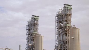 Çimento fabrikası. Ön planda, çimento üretiminde büyük olasılıkla fırın olan birkaç büyük silindirik yapı vardır. Fırınlar büyük, dönen fırınlardır, kireçtaşı ve diğer şeyleri ısıtırlar.