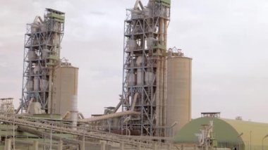 Çimento fabrikası. Ön planda, çimento üretiminde büyük olasılıkla fırın olan birkaç büyük silindirik yapı vardır. Fırınlar büyük, dönen fırınlardır, kireçtaşı ve diğer şeyleri ısıtırlar.