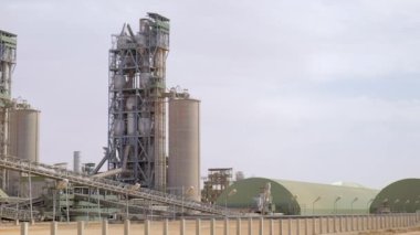 Çimento fabrikası. Ön planda, çimento üretiminde büyük olasılıkla fırın olan birkaç büyük silindirik yapı vardır. Fırınlar büyük, dönen fırınlardır, kireçtaşı ve diğer şeyleri ısıtırlar.