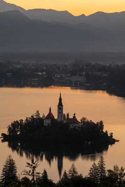 Slovenya. Bled Gölü. Adada gün doğumu gökyüzünün parlak mavisini yansıtan kristal berrak bir göl. Yeşiller yemyeşil dağlar turkuaz suyun etrafını sarmış ve yamaçlarında parlak yeşil noktalar var.