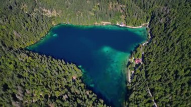 İHA uçuşu. İtalya 'daki Iago Inferiore di Fusine Gölü. Altınızda gökyüzünün renklerini yansıtan büyüleyici bir göl var. Yüzeyi zümrüt yeşili bir renkle parıldıyor.