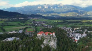 İHA uçuşu. Slovenya. Kanlı Kale. Bled Gölü. Altınızda Bled Gölü var, masmavi gökyüzünü yansıtan bir ayna ve yemyeşil dağlar. Uçurumun tepesinde bir ortaçağ başyapıtı olan Kanlı Kale yükseliyor.
