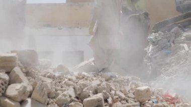 Suudi Arabistan Kazıcı 'daki konut binalarının yıkımı inşaat atıklarını yüklüyor ve taşıyor, işçiler ona yardım ediyor. Bu görüntü, bir yerleşim yerinin yıkıldığı dramatik sahneyi gösteriyor.