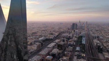 İnsansız uçak zarif bir şekilde Suudi Arabistan, Riyad üzerinde süzülerek görkemli Krallık Kulesi 'ni gün ışığında ele geçirdi. Gün doğumu. Şehir, mimarisinde modernliği yansıtırken, yerin altına yayılır.