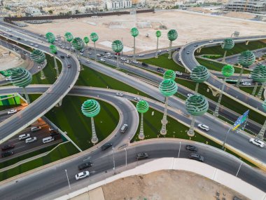 Meşgul otobanın insansız hava aracı fotoğrafı Yeşil Alan Riyad KSA. Bu fotoğraf, Suudi Arabistan 'ın Riyad kentinde arabaların ve kamyonların parlak güneşin altında yol boyunca koştuğu yoğun bir otoyolu yakalar. Otoyol...