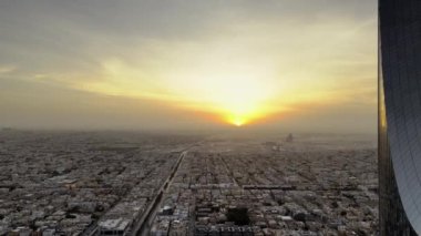İnsansız uçak zarif bir şekilde Suudi Arabistan, Riyad üzerinde süzülerek görkemli Krallık Kulesi 'ni gün ışığında ele geçirdi. Gün doğumu. Şehir, mimarisinde modernliği yansıtırken, yerin altına yayılır.