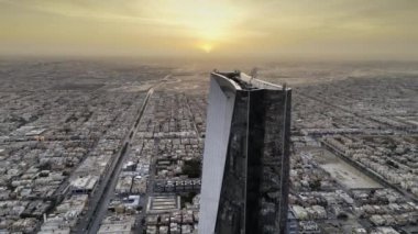 İnsansız uçak zarif bir şekilde Suudi Arabistan, Riyad üzerinde süzülerek görkemli Krallık Kulesi 'ni gün ışığında ele geçirdi. Gün doğumu. Şehir, mimarisinde modernliği yansıtırken, yerin altına yayılır.