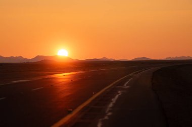 Desert Highway 'de Altın Gün Batımı Sahne Yolu Macerası. Suudi Arabistan. Sonsuz bir çöl yolunda altın ışıkla yıkanmış büyüleyici bir günbatımı. Ufka giden uzun, açık yol.