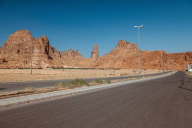 Suudi Arabistan 'daki Alulas Majestic Rock Formasyonları' ndan geçen Manzaralı Yol. AlUla, Suudi Arabistan 'ın nefes kesici kaya oluşumları boyunca uzanan çarpıcı, iyi döşenmiş bir yol. Bu resim görüntüyü yakalar