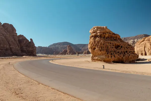 Suudi Arabistan 'daki Alulas Majestic Rock Formasyonları' ndan geçen Manzaralı Yol. AlUla, Suudi Arabistan 'ın nefes kesici kaya oluşumları boyunca uzanan çarpıcı, iyi döşenmiş bir yol. Bu resim görüntüyü yakalar
