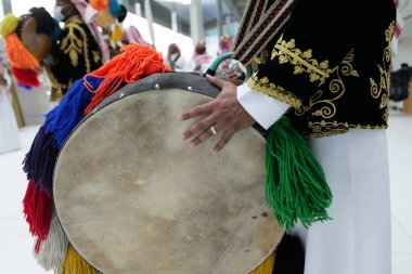 Geleneksel Suudi Arabistan Davul Performansı - Kültürel Kutlama. Geleneksel Suudi Arabistan davulunu çalan siyah ve altın işlemeli bir elbise giymiş bir müzisyenin yakın çekimi. Davul.