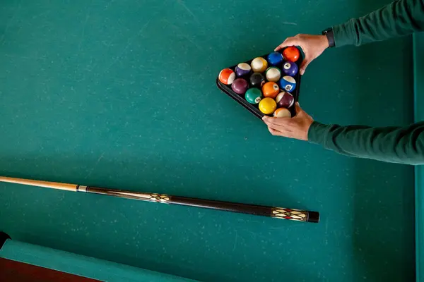 Bilardo oyunu kurulumu. KSA. Eğlenceliydi. Bir oyuncu bilardo oyununa hazırlanmak için yeşil keçeli bilardo masasında üçgen bir rafta bilardo topları düzenliyor. Yakınlarda bir tahta ıstaka duruyor, kırılmaya hazır.