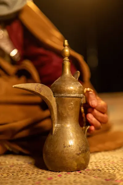 Suudi Arabistan 'da geleneksel Bedevi misafirperverliği. Çölde örülmüş bir halıda oturan bir Bedevi 'nin yakın çekimi, yanında geleneksel bir Arap kahve cezvesi olan Dallah. Bu sahne mükemmel.
