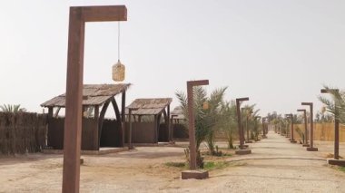 Suudi Arabistan 'da açık hava feneri. Video kaydı. Çölde palmiye ağaçları ve geleneksel ahşap fenerlerle çevrili pitoresk bir yürüyüş. Zarif beyaz kolye ışıkları sıcak ve davetkar bir ışık yaratır.