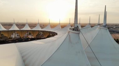 Riyad Stadyumu 'nun gündoğumunun hava görüntüsü. Güneş doğarken Suudi Arabistan 'ın Riyad kentindeki ikonik stadyumu gösteren sakin bir hava manzarası. Yapının eşsiz beyaz, çadırımsı çatısı.