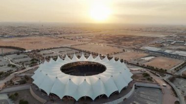 Riyad Stadyumu 'nun gündoğumunun hava görüntüsü. Güneş doğarken Suudi Arabistan 'ın Riyad kentindeki ikonik stadyumu gösteren sakin bir hava manzarası. Yapının eşsiz beyaz, çadırımsı çatısı.
