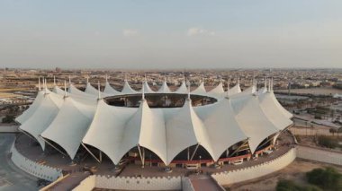 Riyad Stadyumu 'nun gündoğumunun hava görüntüsü. Güneş doğarken Suudi Arabistan 'ın Riyad kentindeki ikonik stadyumu gösteren sakin bir hava manzarası. Yapının eşsiz beyaz, çadırımsı çatısı.