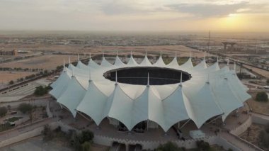 Riyad Stadyumu 'nun gündoğumunun hava görüntüsü. Güneş doğarken Suudi Arabistan 'ın Riyad kentindeki ikonik stadyumu gösteren sakin bir hava manzarası. Yapının eşsiz beyaz, çadırımsı çatısı.