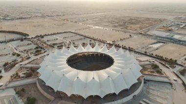 Riyad Stadyumu 'nun gündoğumunun hava görüntüsü. Güneş doğarken Suudi Arabistan 'ın Riyad kentindeki ikonik stadyumu gösteren sakin bir hava manzarası. Yapının eşsiz beyaz, çadırımsı çatısı.