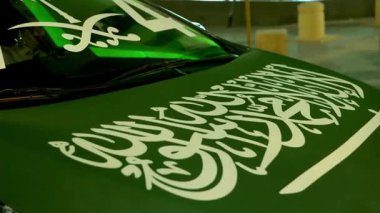 Suudi Araç Günü Dekorasyonu. Ulusal Günü kutlamak için Suudi Arabistan bayrağı ve ulusal sembollerle süslenmiş bir arabanın yakın plan görüntüsü. Yeşil tema, palmiye, kılıç ve Arapça.