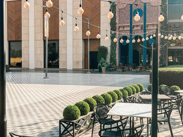 U-Walk Riyad 'da String Lights ile Modern Açık Cafe. U-Walk, Riyad, Suudi Arabistan 'da nefis bir açık hava yemek düzeni. Mermer kaplama masalar ve dekoratif yeşil çalılar zarif bir iple çerçevelenir.