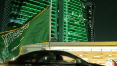 Ulusal Bayram kutlamalarında Suudi Bayrağı Gece Dalgalanıyor. Suudi Arabistan bayrağının yakın çekimleri Ulusal Bayram 'ı simgeleyen yeşil ışıklarla süslenmiş aydınlanmış bir kulenin önünde gururla dalgalanıyor.