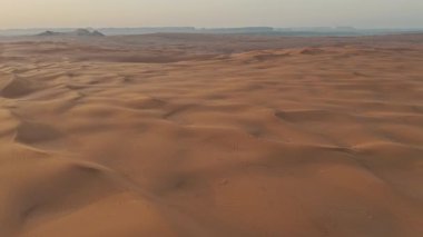 Suudi Çölü 'nde Gündoğumu Drone tarafından yakalandı. Yükselen güneşin altın ışınları bu nefes kesici hava manzarasında Suudi çölünün kayan kumullarını aydınlatıyor. Manzaranın pürüzsüz kıvrımları
