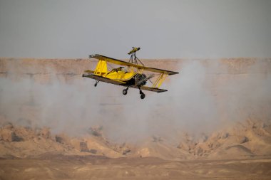 Wingwalker KSA Hava Gösterisi 'nde Suudi Çölü Havacılık Daring' in üstünde uçuyor. Korkusuz bir kanat yürüyüşçüsü, bir havacılık gösterisi sırasında çölde süzülen klasik sarı bir çift kanatlı uçağın tepesinde nefes kesici bir gösteri sergiliyor.