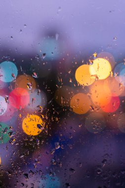 Mavi cam arka planda yağmur damlaları. Şehir sokak lambaları bokeh odağını kaybetti, soyut alacakaranlık şehri arka planı