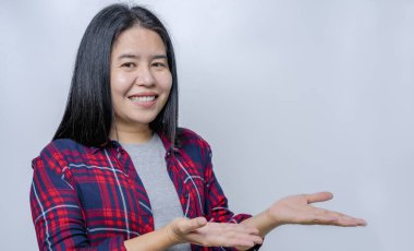 Portrait of adult Asian lady smiling with cheerful expression, shows something amazing at blank space in casual clothing and standing isolated over grey background. Facial expression concept.  
