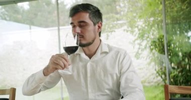 Sommelier şarap kadehini sallıyor ve tadına bakıyor. Zarif giyimli adam bir tat alıyor ve şeffaf bardağa dökülen taze kırmızı şarabı içiyor..