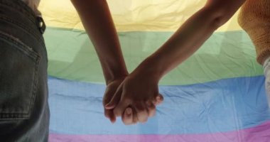 Kızların elleri LGBT bayrağına yaklaşıyor. Sarılın ve birbirinize sarılın. LGBT Love, lezbiyen çift eğleniyor. Sevgi ve desteği paylaşan iki kadın el ele tutuşuyor. Yaşam tarzı ve ilişkiler.