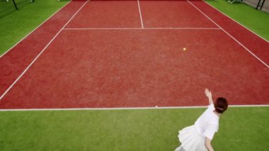 Arkadaşlar dışarıda halı kortlarında tenis oynarlar. Aktif boş zaman oyunu. Havadan, yukarıdan aşağıya, İHA atışı. Bir kadın profesyonel ve dinamik olarak yavaş çekimde tenis oynar. Arkadaşlarla aktif spor oyunu.