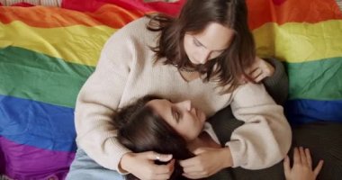 Evdeki güzel kızlar yatak odasında öpüşüyor. Lgbt lezbiyen kadınları gurur bayrağıyla evde dinleniyor. Sarılın ve birbirinize sarılın. Aşk ve öpücük, LGBT hakları, yaşam tarzı ve ilişkiler. LGBT kavramı