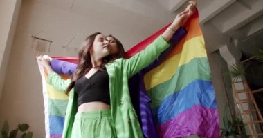 Birbirinizi gökkuşağı bayrağıyla kucaklayın ve tutun. Aşk ve öpücük, LGBT Gurur Ayı, arkadaşlık konsepti. Lgbt kadınları evde dinleniyor. Sevgi ve desteği paylaşan iki kadın el ele tutuşuyor.