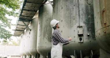 Erkek şarap imalatçısı, içeceklerin kalitesini içeride kontrol ediyor ve günlüğe tarihleri yazıyor. Modern şarap imalathanesi veya şarap imalathanesi. Şarap fermantasyonu için büyük çelik fıçılar..