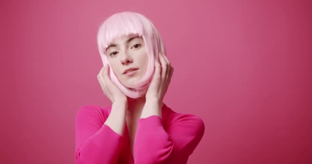 美しい目 ピンクの白い髪とピンクの服を持つ美しさの女性 髪を手配し 自分自身を美しくし 孤立したピンクの背景にカメラを見てください 官能的な魅力的な女性モデルのポーズ — ストック動画