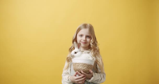 Dziewczynka Białej Sukience Trzyma Kosz Królikiem Dłoni Odizolowanym Żółtym Tle — Wideo stockowe