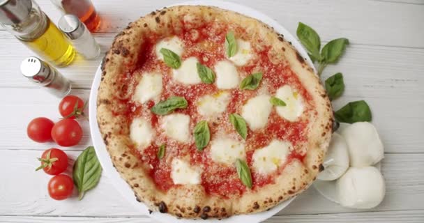 用番茄酱 莫扎拉乳酪和新鲜罗勒旋转在厨房配料旁边的木制桌子上的白盘开胃的新鲜披萨马盖里塔的头像 — 图库视频影像