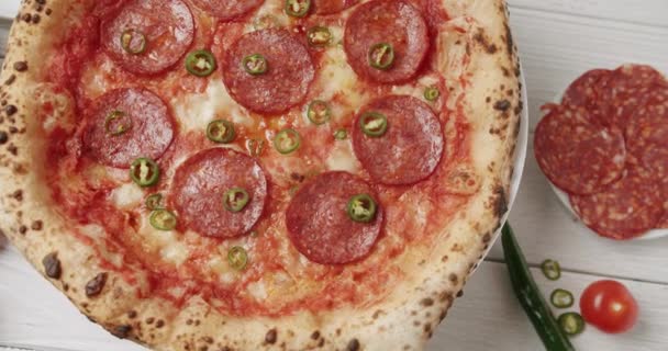 从上面的美味自制意大利披萨番茄酱 意大利腊肠和绿色辣椒旋转盘放在厨房的白色木制桌子上 美味的新鲜烤披萨 — 图库视频影像