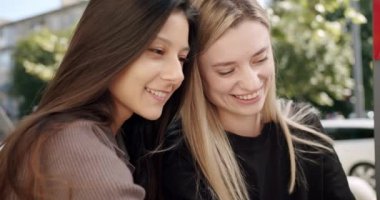 Neşeli kız arkadaşlar sokak kafesinde vakit geçiriyorlar. Yaz günü sokak kafeteryasında vakit geçirirken gülümsemek ve birbirleriyle konuşmak için kahveyle el kamerasıyla çekilmiş mutlu genç kadınlar.