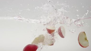 Temiz suya düşen elma parçaları. Beyaz arkaplanlı şeffaf temiz suyun yavaş hareketli durağan görüntüsü ve olgun kırmızı elma parçalarından dökülen parçacıklar.