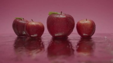 Su yüzeyinde yuvarlanan elmalar. Bütün kırmızı elmaları yüzeye yuvarlarken, kırmızı elmalara ve yumuşak ışıkta pembe arkaplana su sıçratırken statik görüntü.