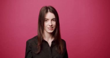 Kamerayla flört eden şık, genç bir esmer. Siyah gömlekli genç bir kadın uzun siyah saçlara dokunuyor ve pembe arka planda kamerayla flört ederken gülümsüyor.