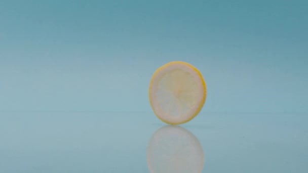 新鮮なレモンの圧延スライス スタティックショットの鮮やかな黄色のカットスライスの新鮮なレモンがミラー表面に圧延と青のスタジオの背景 — ストック動画