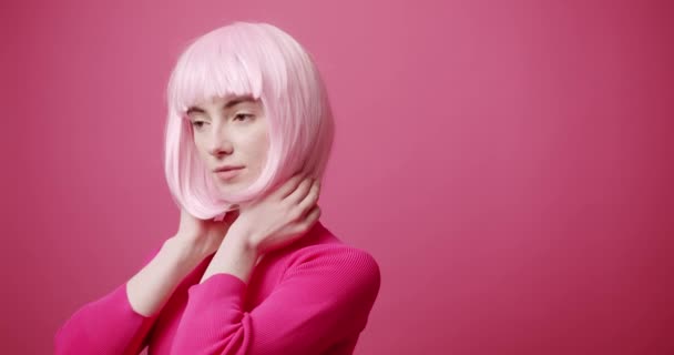 短いピンクの髪に触れる若い女性 短い染めの髪に触れるスタイリッシュな服の若い女性モデルの静的なショットとピンクの背景に目を離して — ストック動画