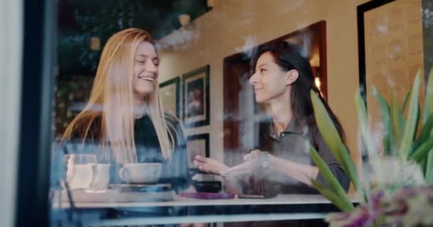 女友们在咖啡店聊天 照片中的年轻女子坐在餐厅餐桌后面 一边向乐观的金发女友摆姿势一边讲故事 — 图库视频影像