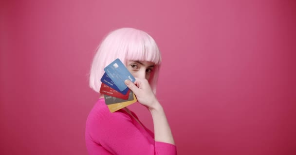 クレジットカードを見せる若い女性 若いです女性銀行クライアントの静的なショットとともに明るい髪デモンストレーション束のカラフルなクレジットカードに対してピンクの背景 — ストック動画