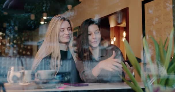 若い女性がカフェで自撮り 幸せな若い彼女の手によるショット笑顔と一緒にスマートフォンを介して自撮りしながら 週末の日にガラスの後ろのカフェテリアテーブルに座って — ストック動画